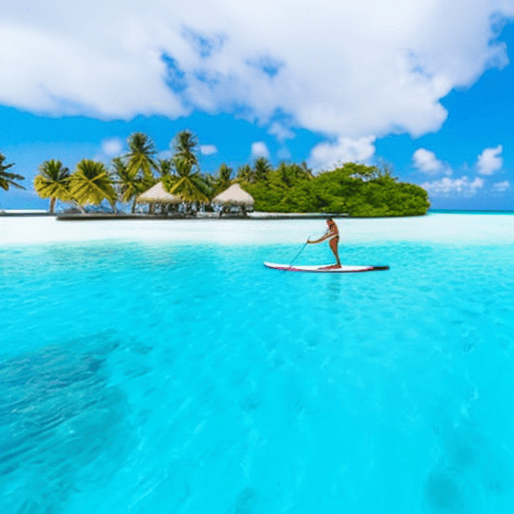 A person paddle-boarding in the crystal clear waters of the Maldives, with a beautiful island in the background
